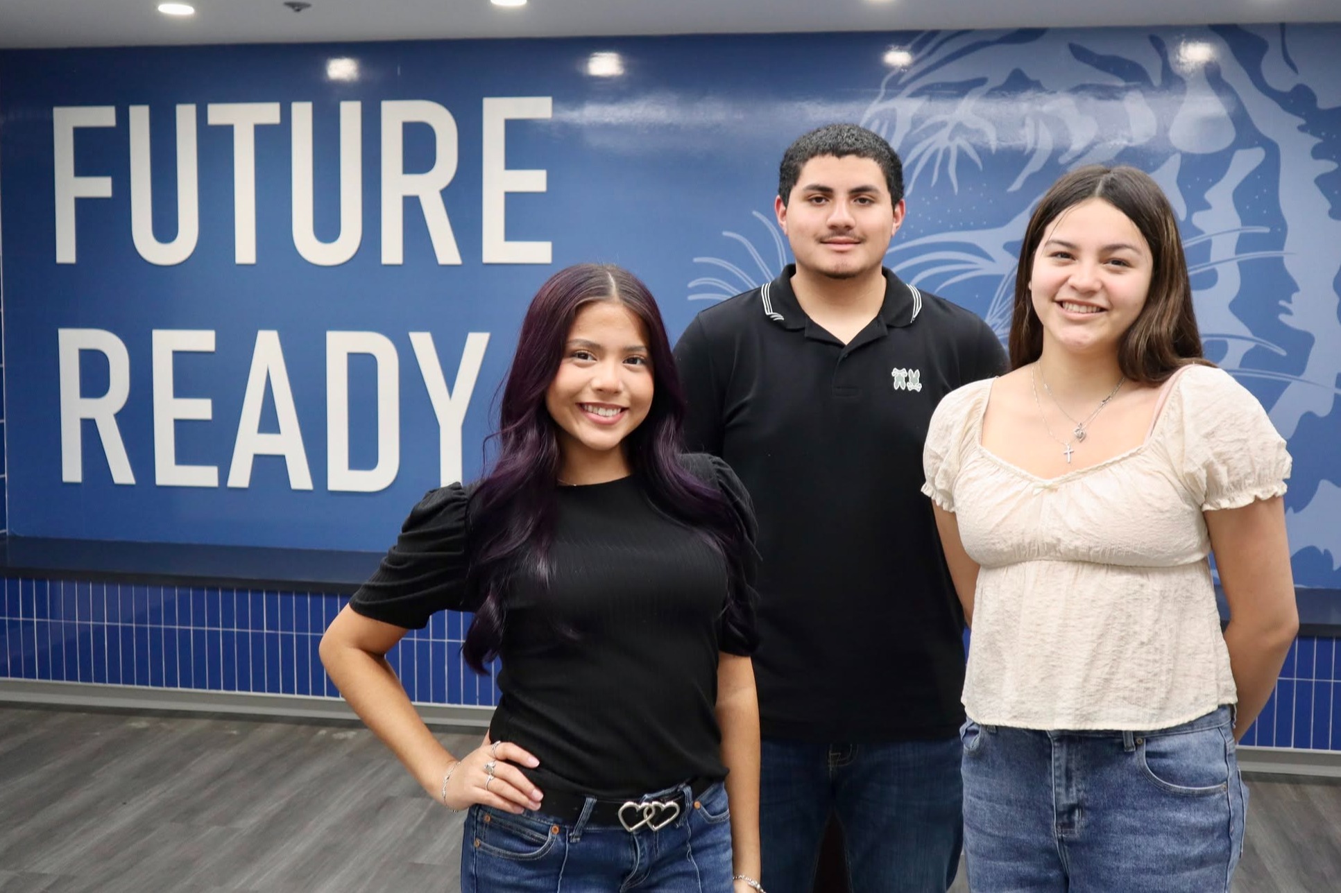 Three students standing in front of blue background with "Future Ready" sign.