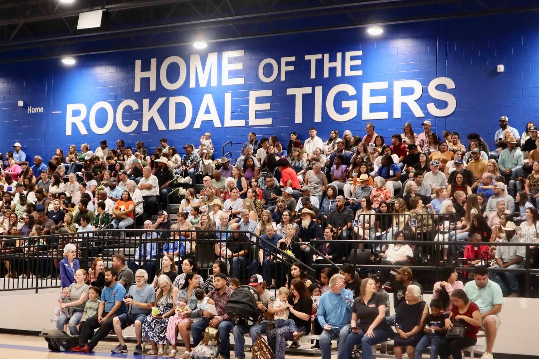 Picture of crowd in gym bleachers with "Home of the Rockdale Tigers" sign above them