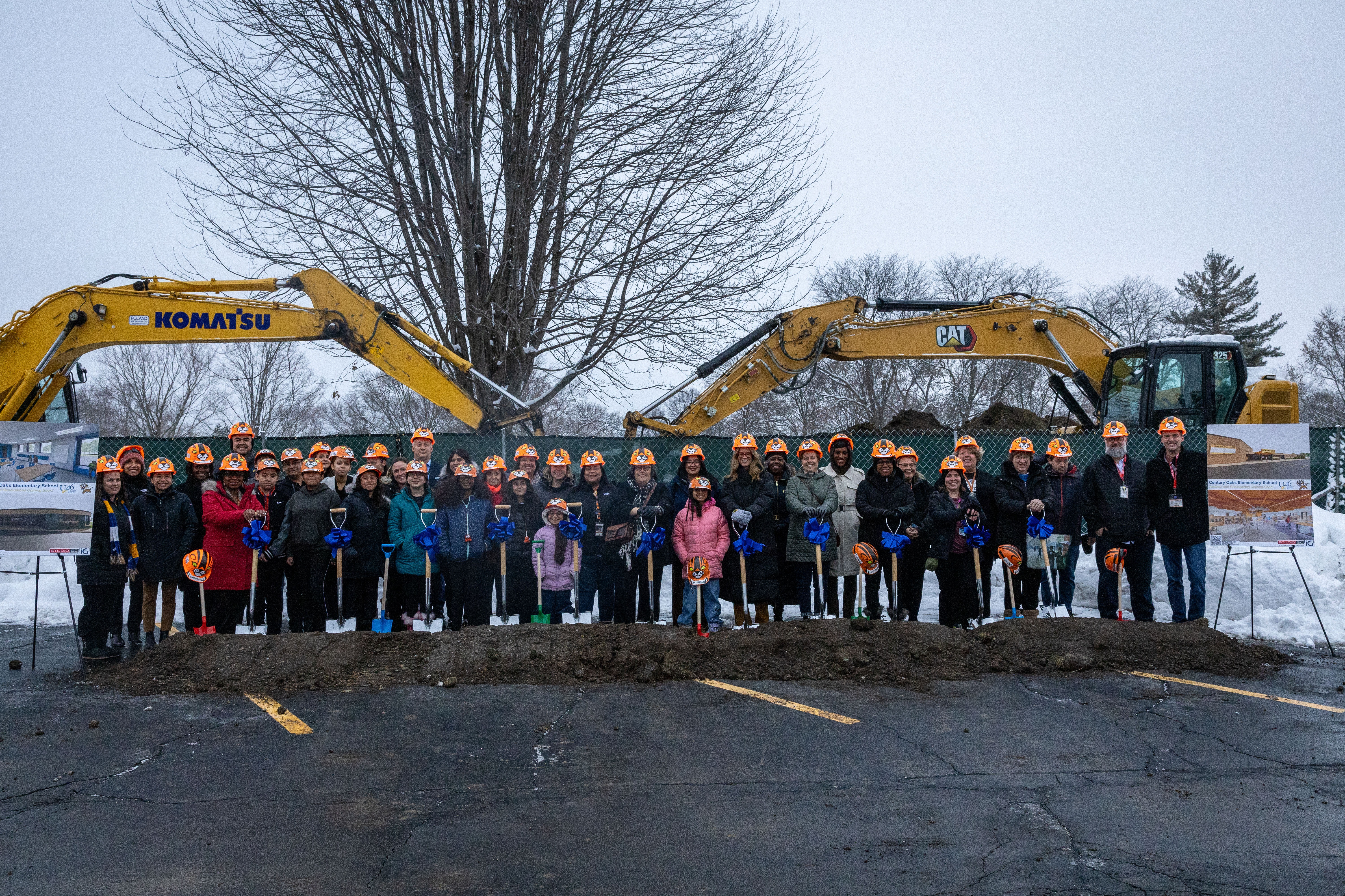 A group gathers in front of construction machinery, wearing hard hats. Snow covers the ground.