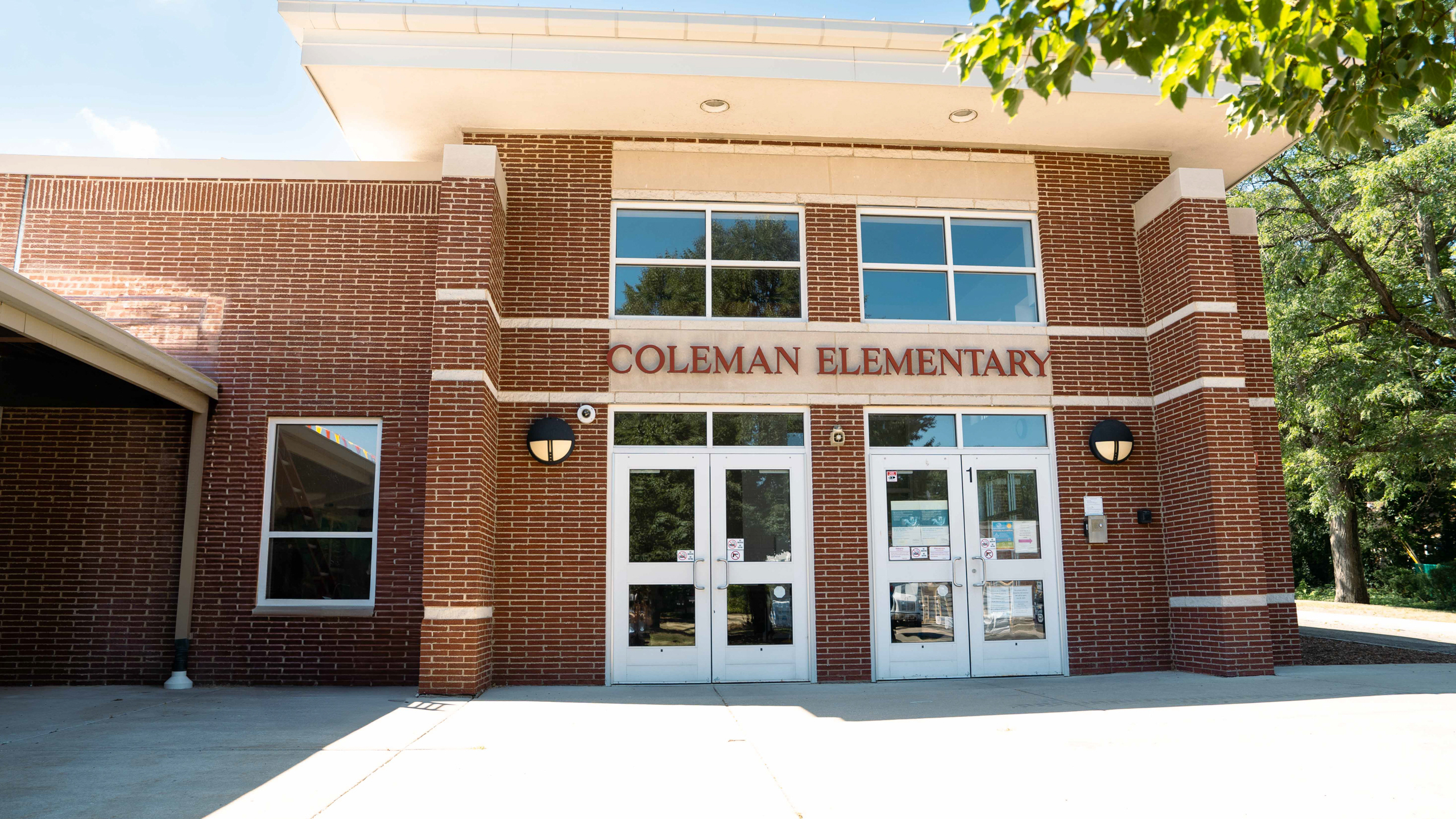 Red brick building with "Coleman Elementary" above the doors, flanked by trees, under a blue sky.