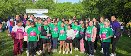 A group of people in green t-shirts, some with bibs, standing together in a park.