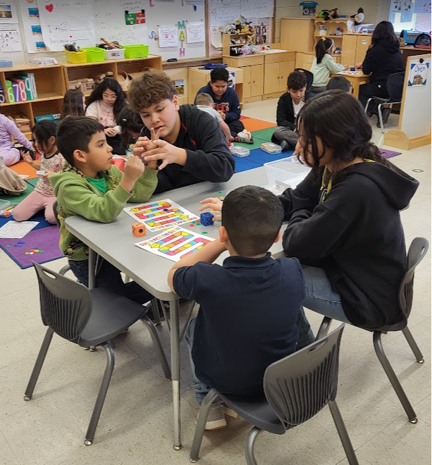 A group of children are sitting around a table in a classroom, playing a board game.