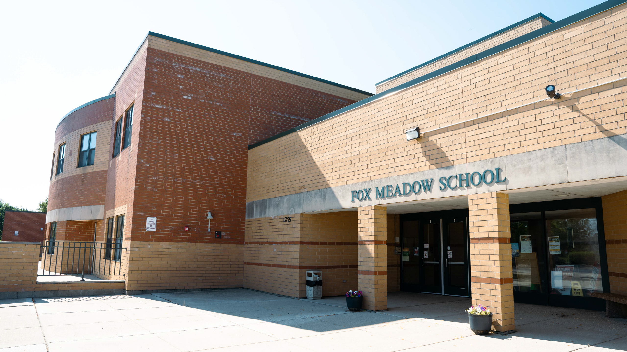 A building with "FOX MEADOW SCHOOL" written on the front and two potted plants in front of the entrance.