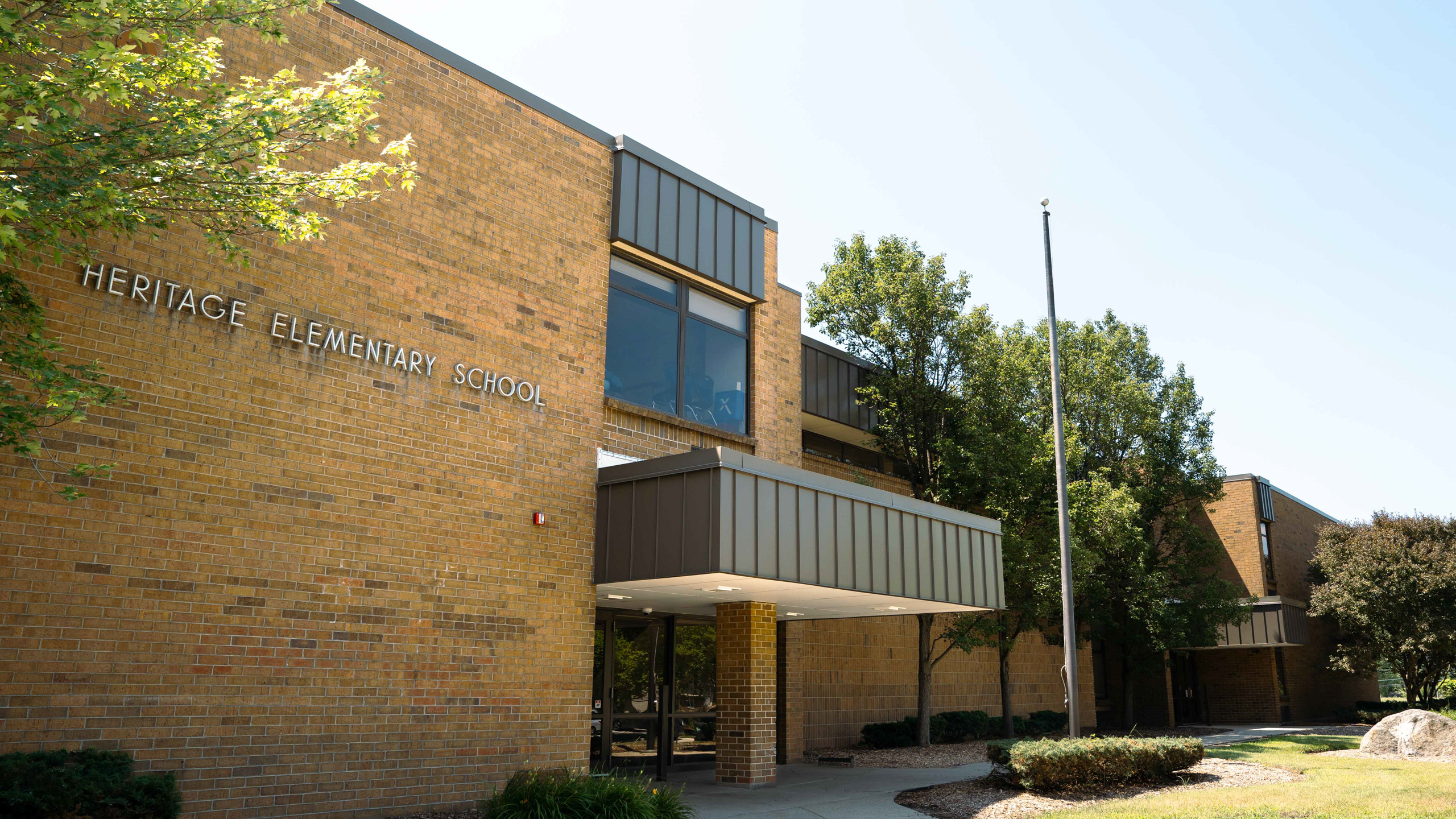 Entrance to a brick building with "HERITAGE ELEMENTARY SCHOOL" sign. Overcast sky in the background.