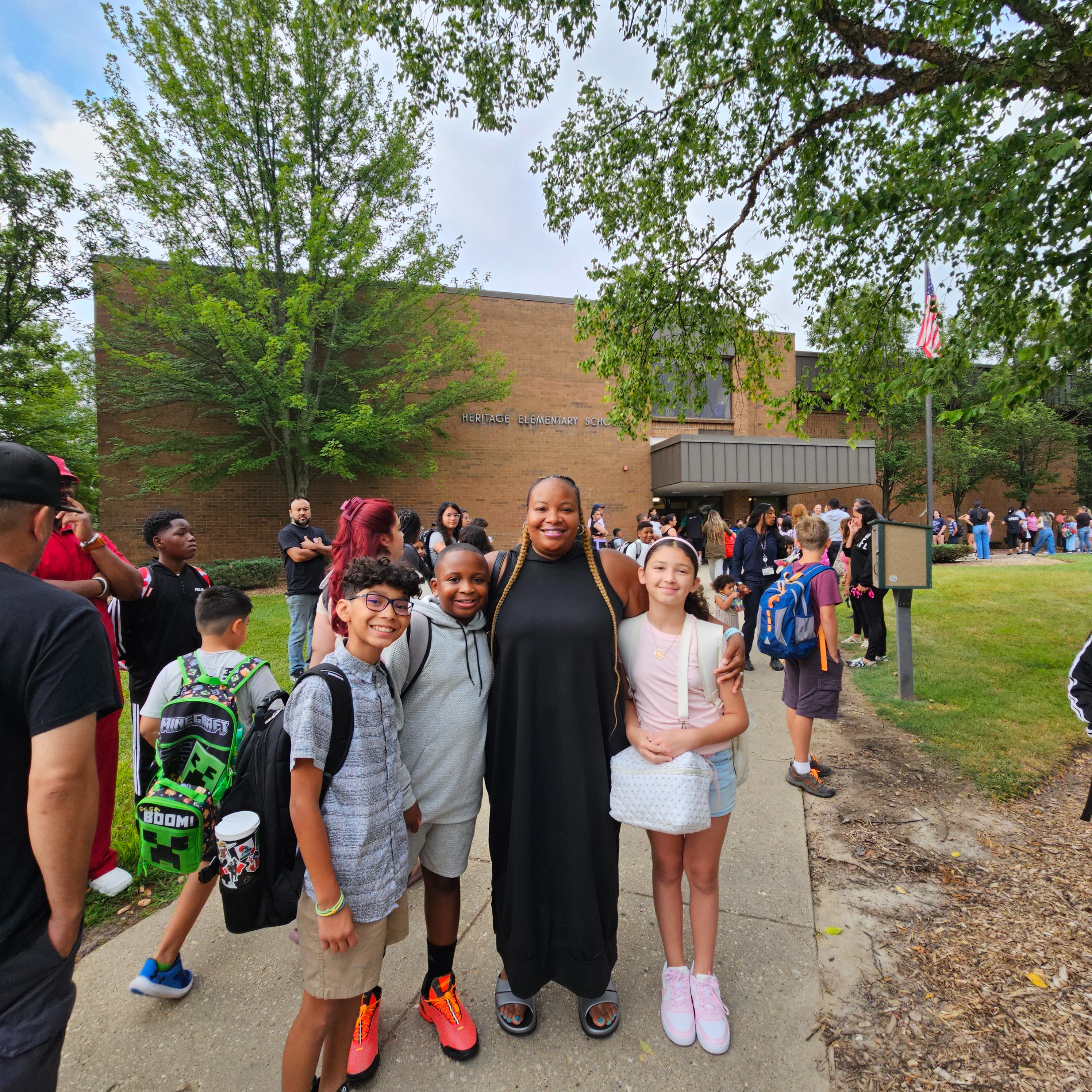 People, including children and adults, gather outside a building with trees and grass, posing for a photo.