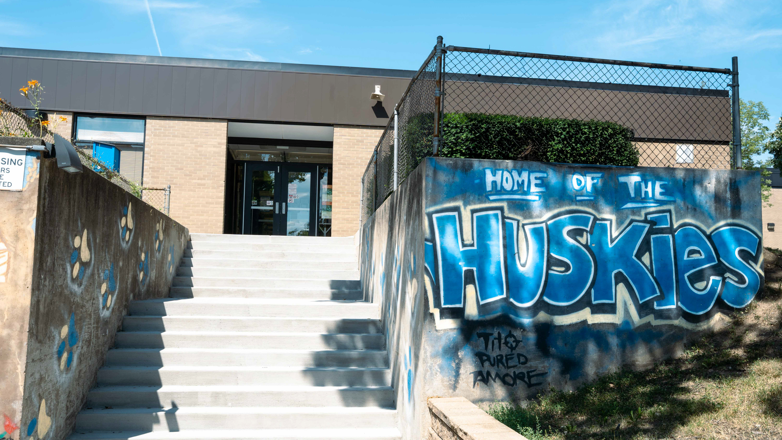 A building entrance with stairs and graffiti that says "Home of the Huskies" on the wall.