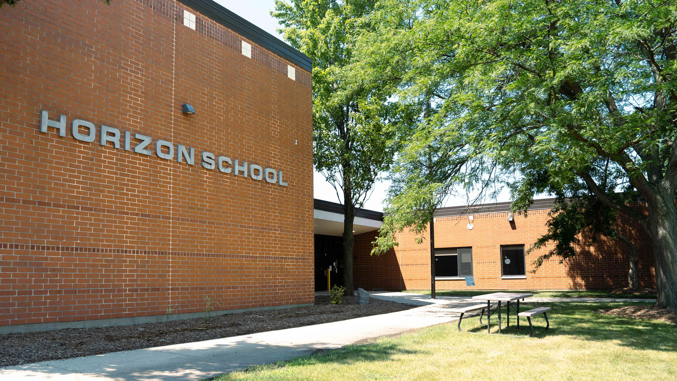 Horizon School's brick building has large windows. A tree is near the entrance. A walkway leads to the entrance.