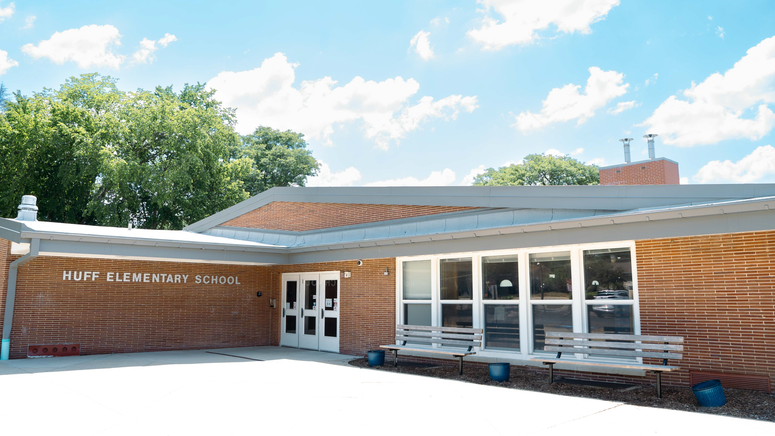 Exterior of Huff Elementary School. A brick building with a gray roof. Two benches on the side.