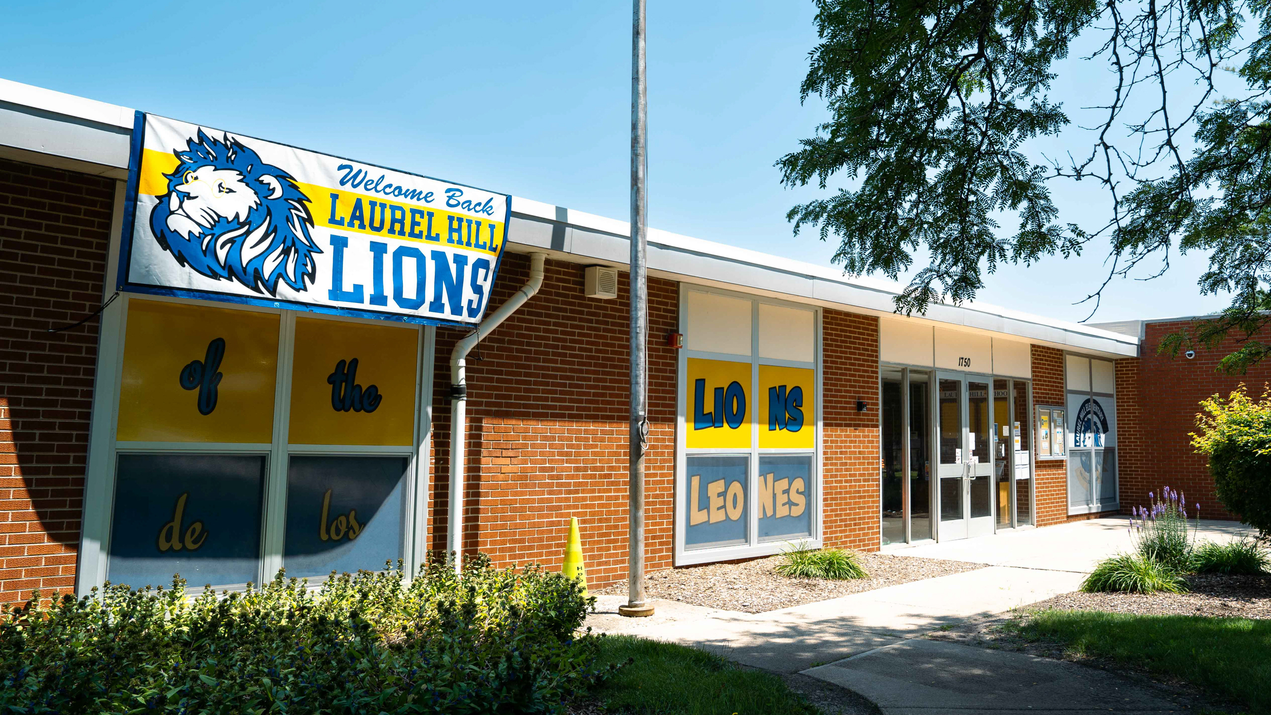 Front of a building with a blue lion logo and "Laurel Hill Lions" text. Brick walls, glass windows, and plants.
