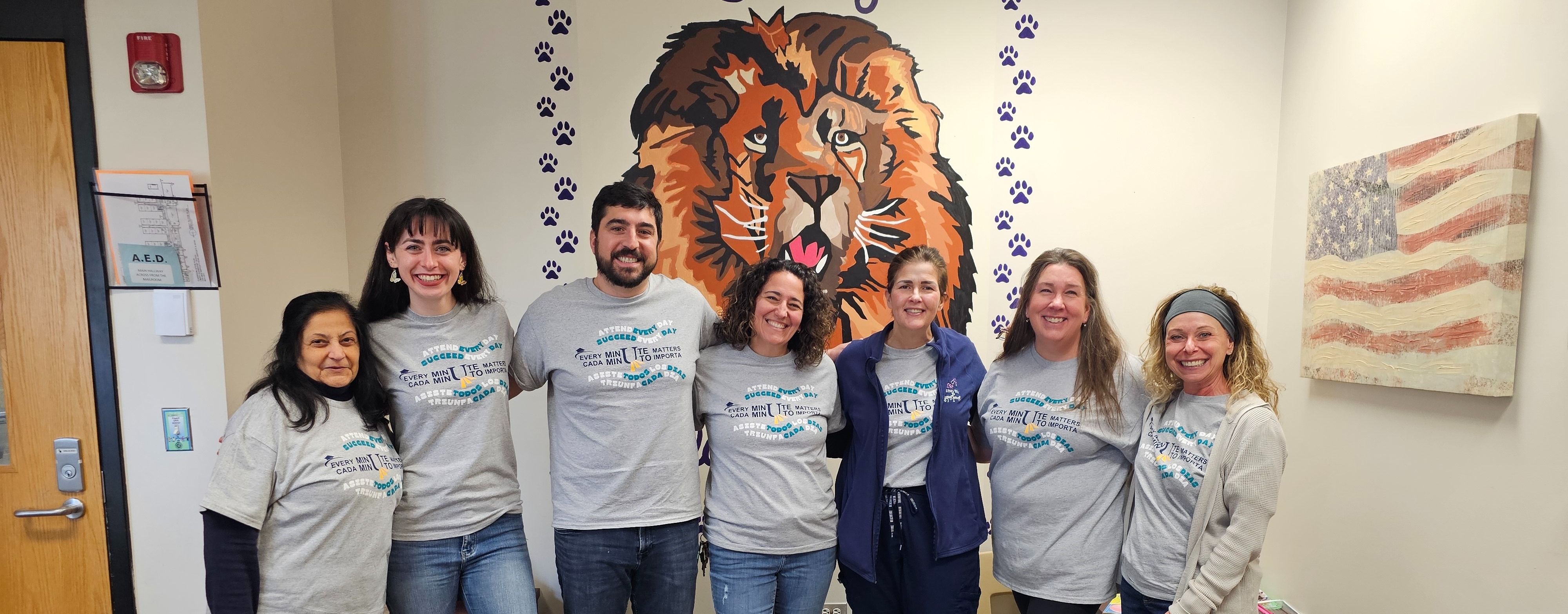 Group of people in matching shirts, smiling, standing in front of a wall with a lion and paw prints.