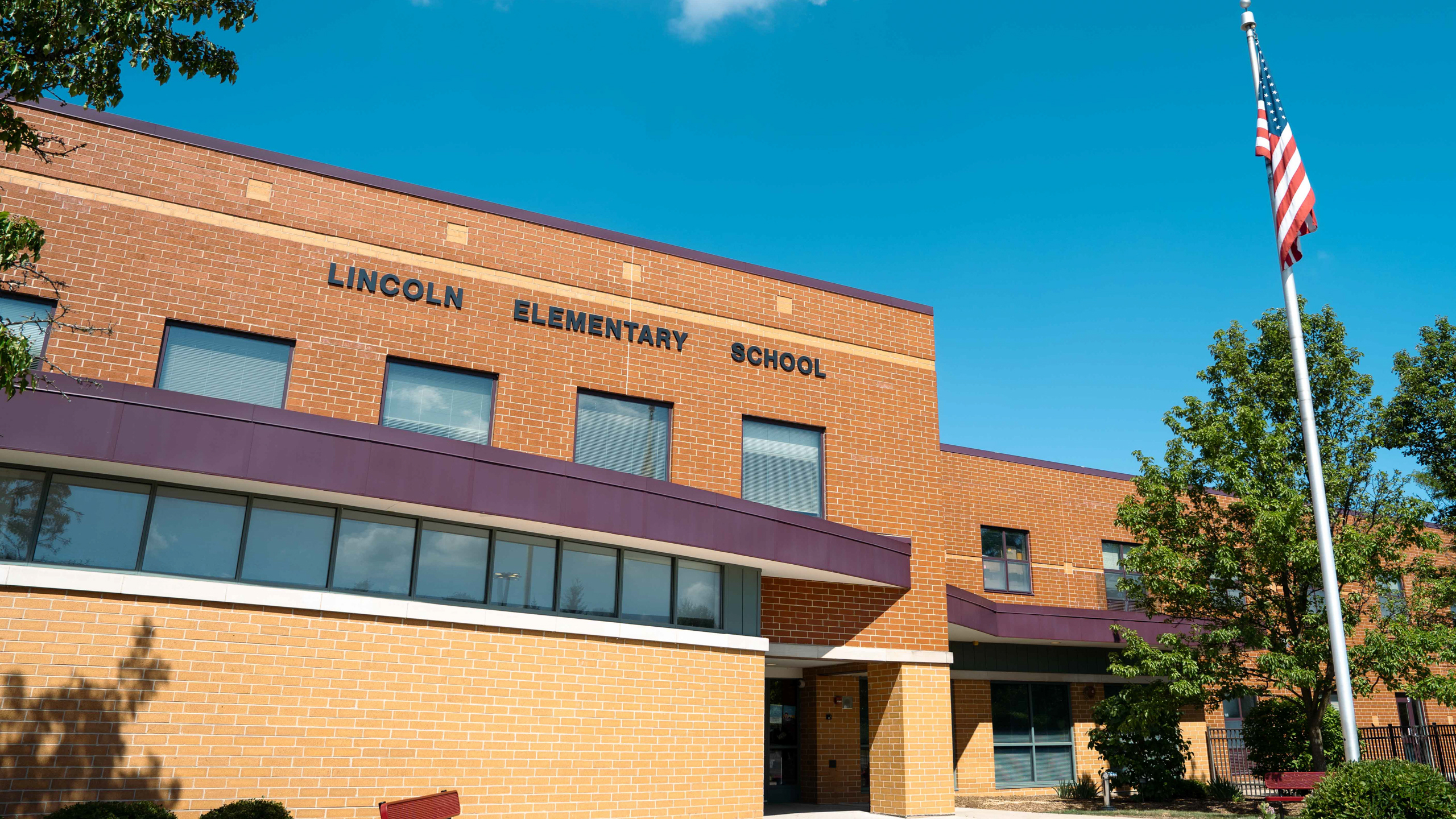 An elementary school with brick walls and glass windows. The name reads "LINCOLN ELEMENTARY SCHOOL". An American flag is on a pole.