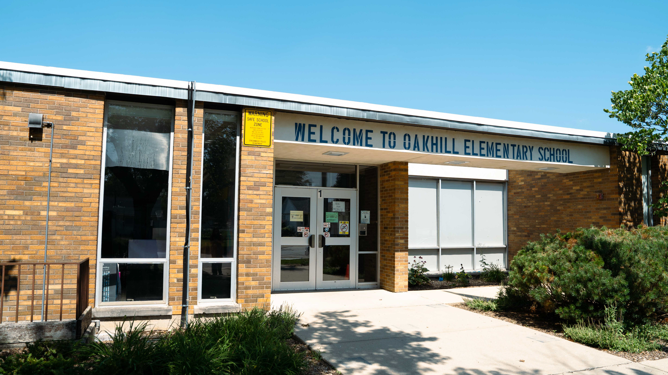 A building with "Welcome to Oakhill Elementary School" on the front. Brick walls, glass windows, and doors.