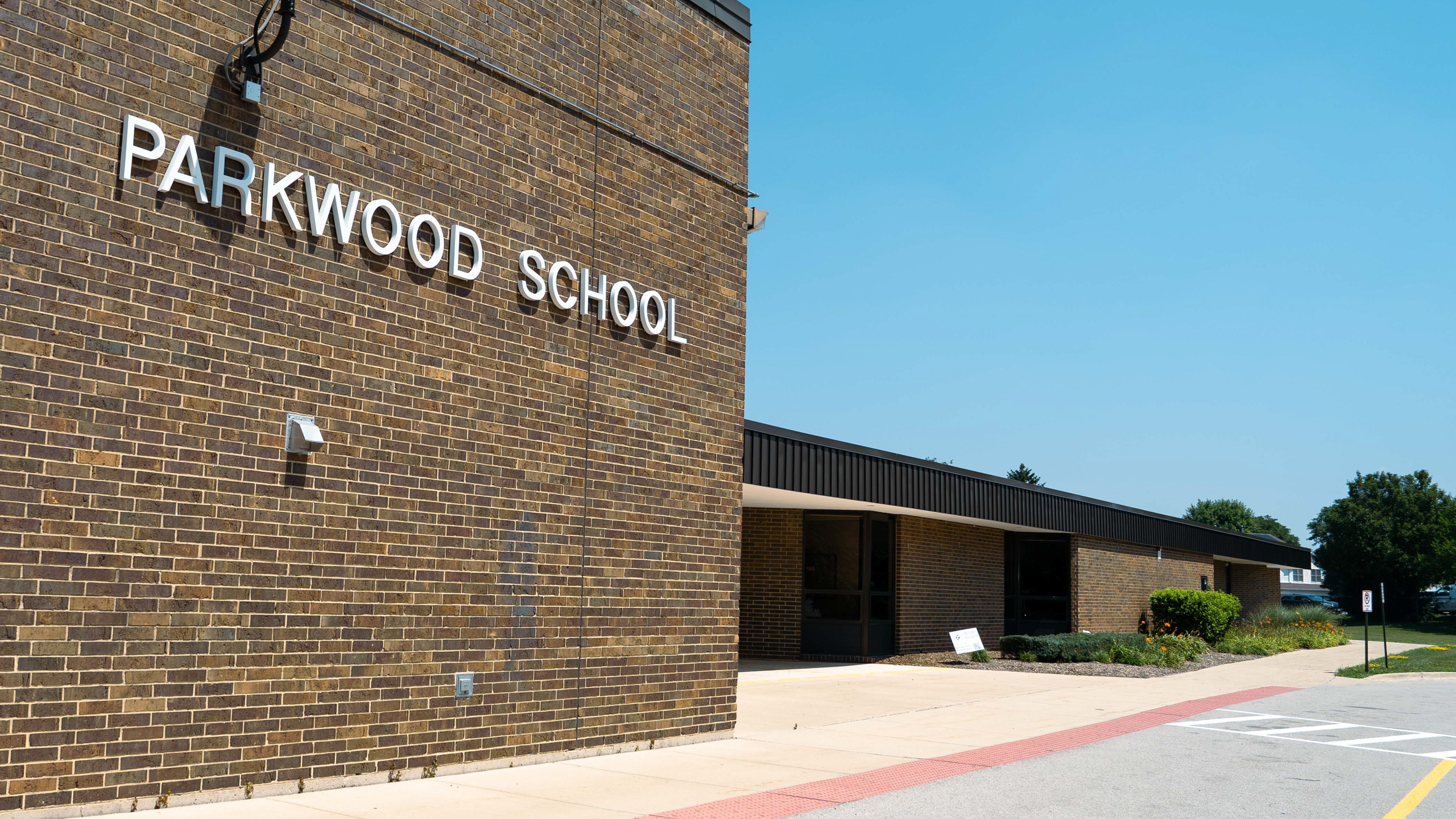A brick wall with "PARKWOOD SCHOOL" on it, and a building in the background under a clear blue sky.