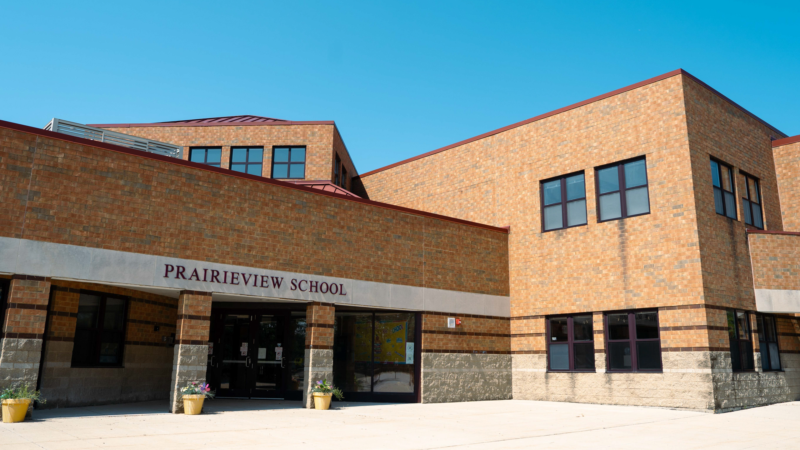 A brick school building with "Prairieview School" written above the entrance. Four yellow planters stand in front.