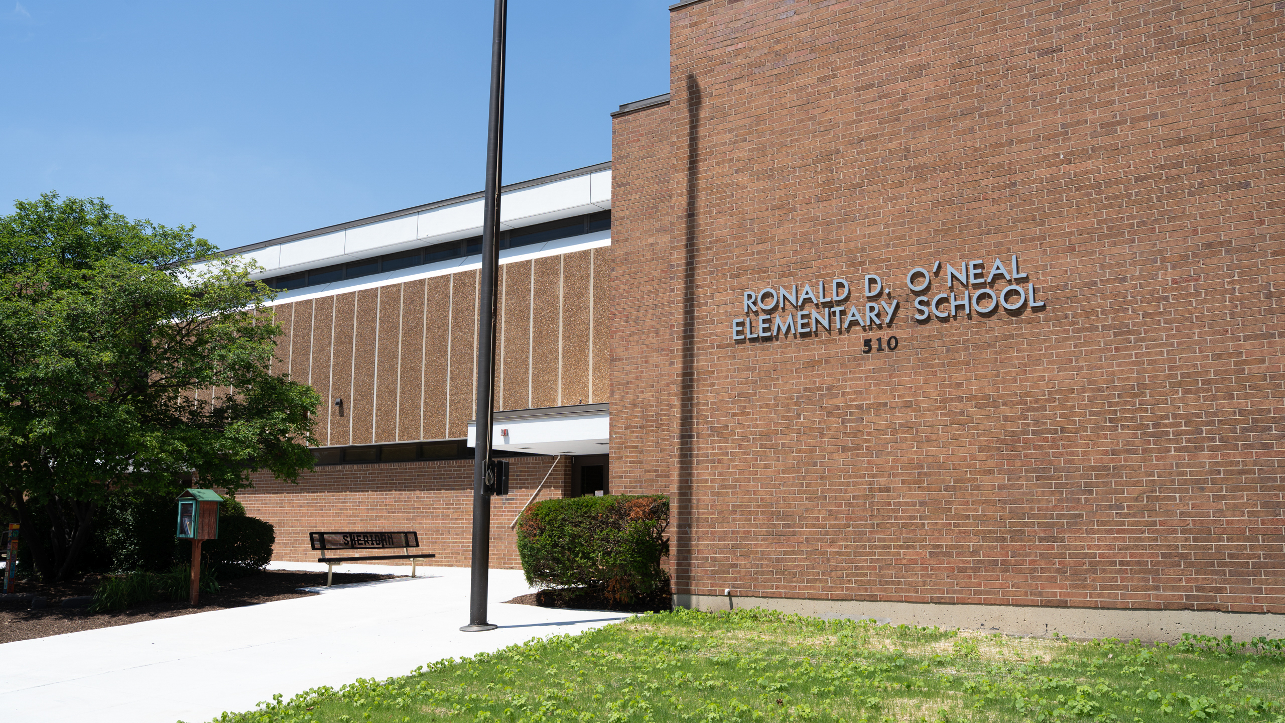 A building with "RONALD D. O'NEAL ELEMENTARY SCHOOL" on it. A bench and a tree are in front.