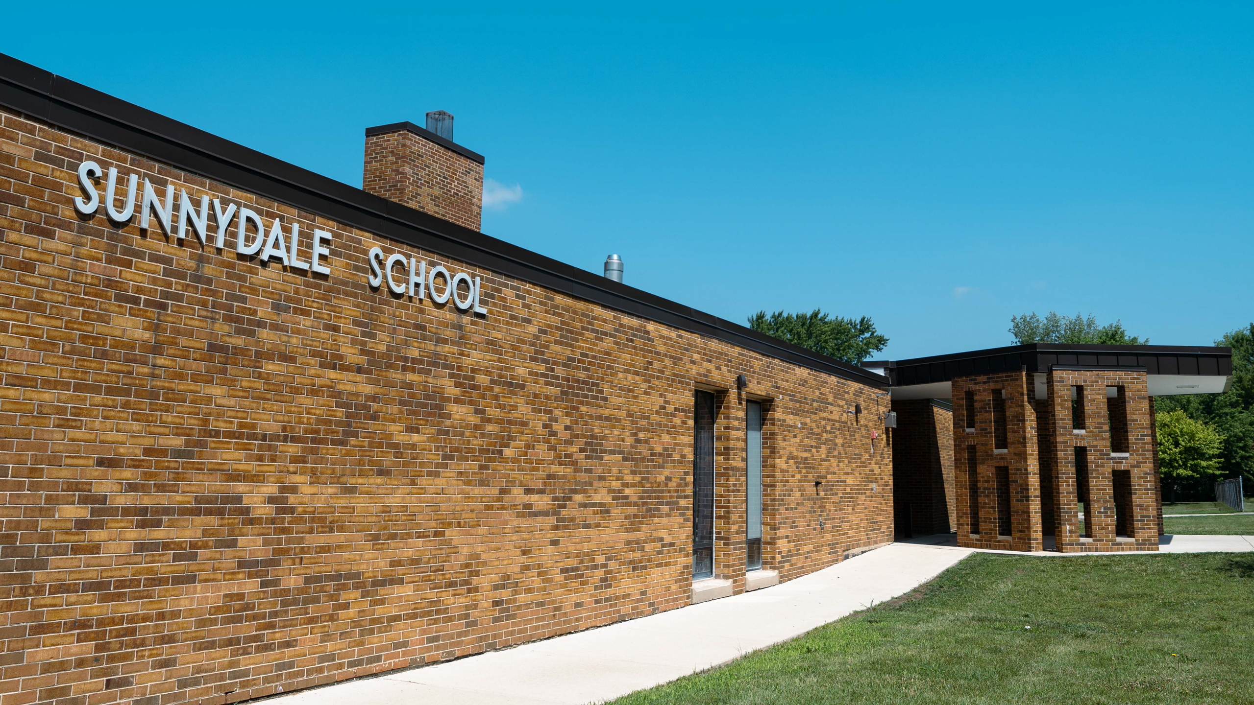 Sunnydale School exterior with brick walls, a brick chimney, a walkway, and a grassy field.