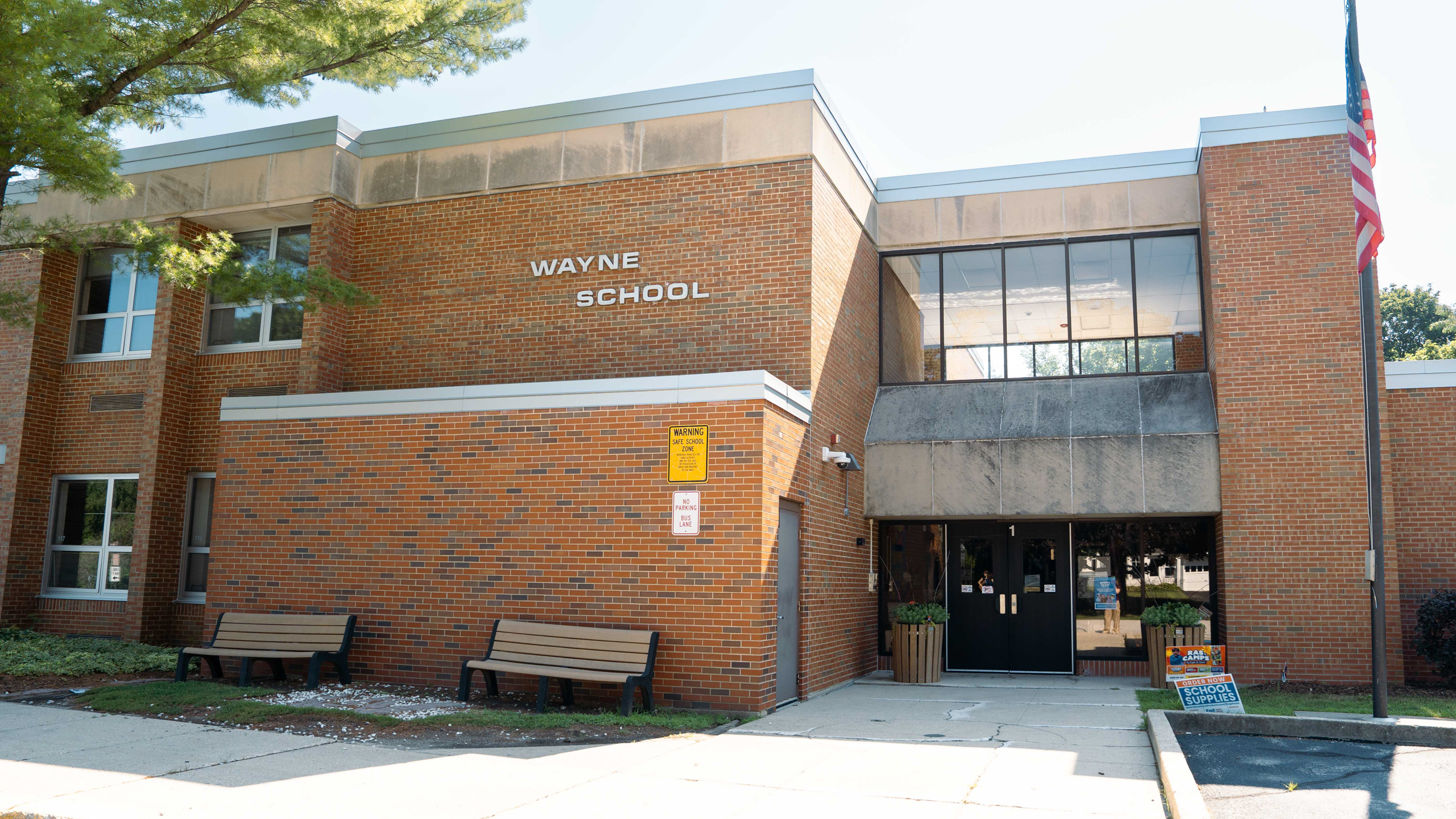 Exterior of Wayne School, brick building with two benches and flag pole in front.