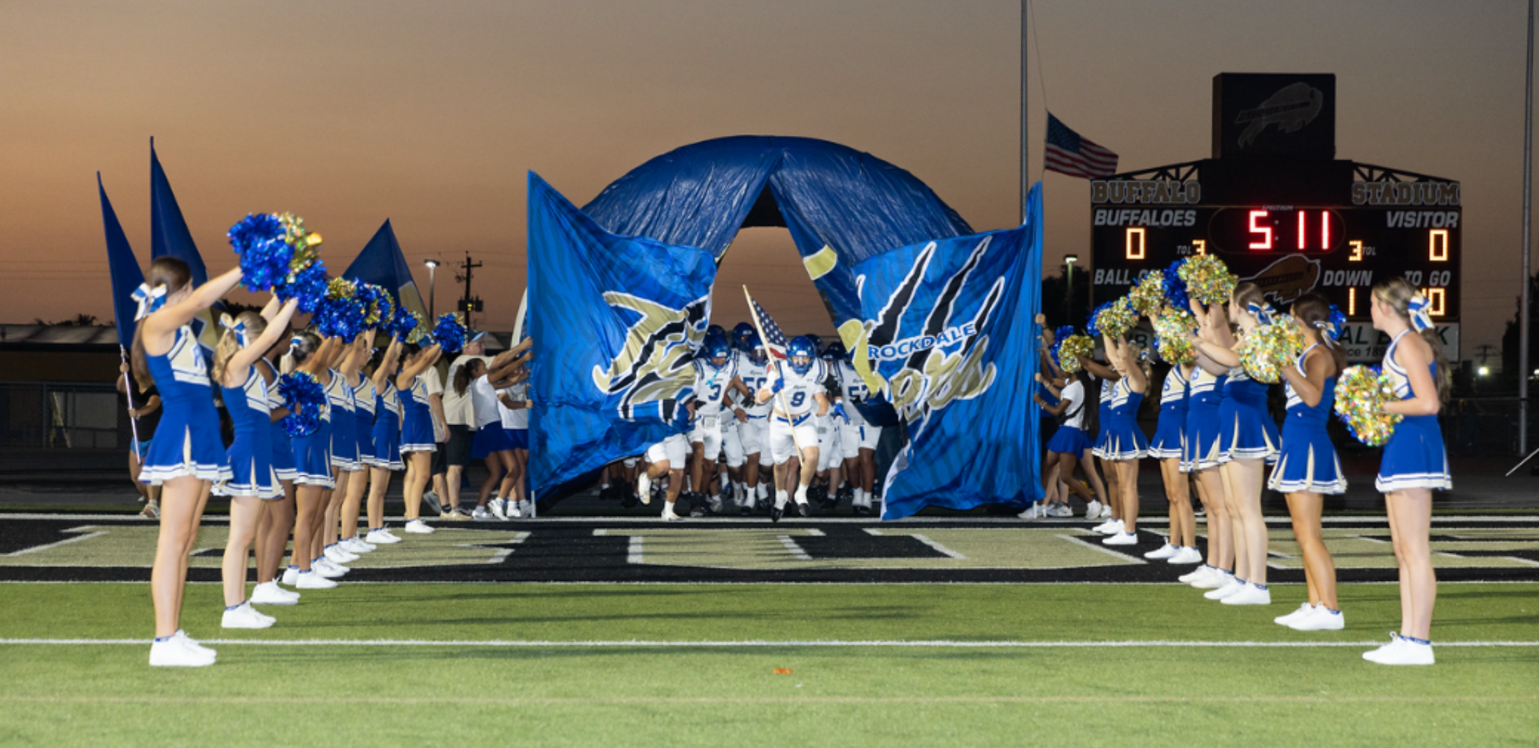 Football team tearing through banner with cheerleaders on either side of the tunnel