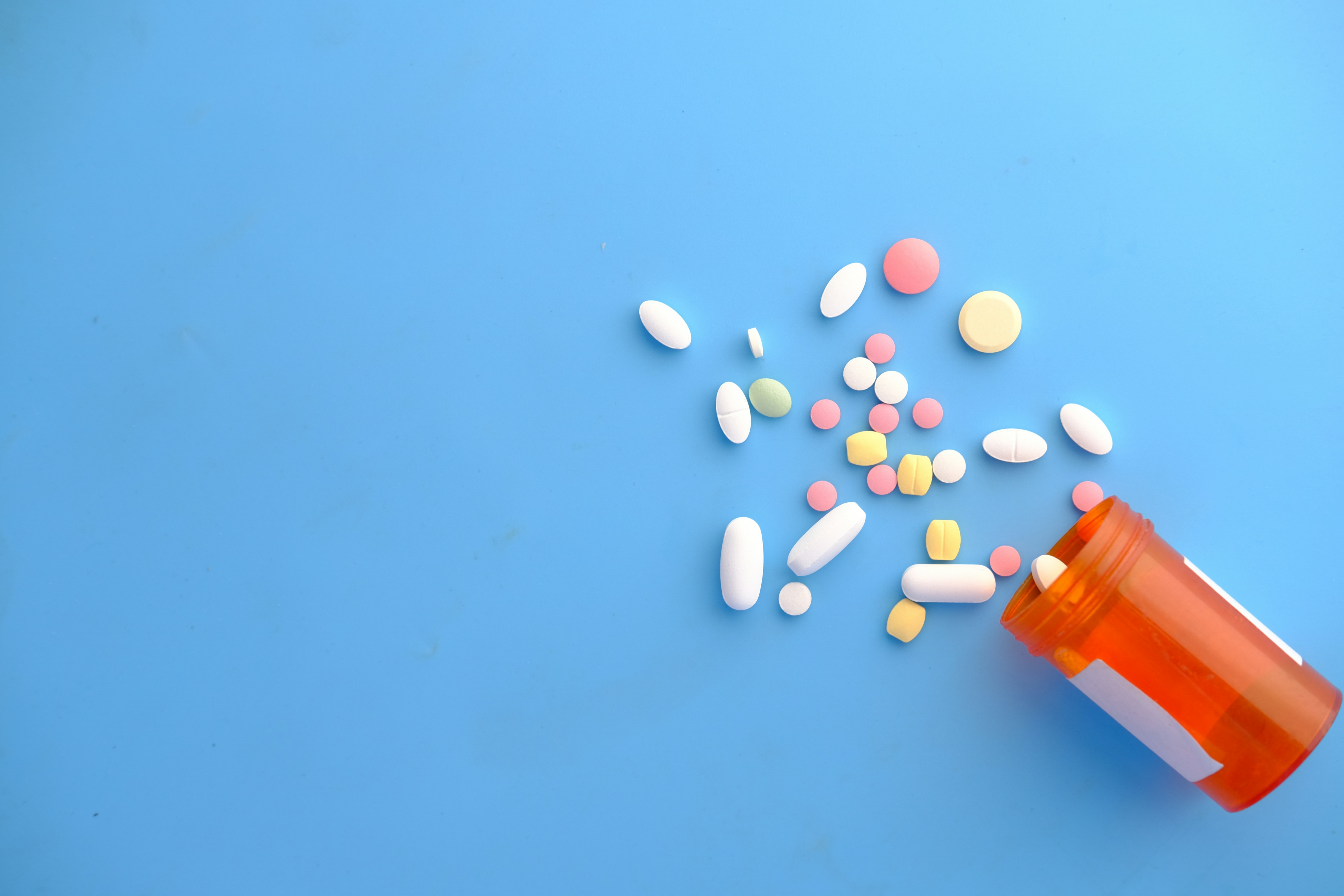 Scattered pills in various colors and sizes on a blue background, with an open orange pill bottle.