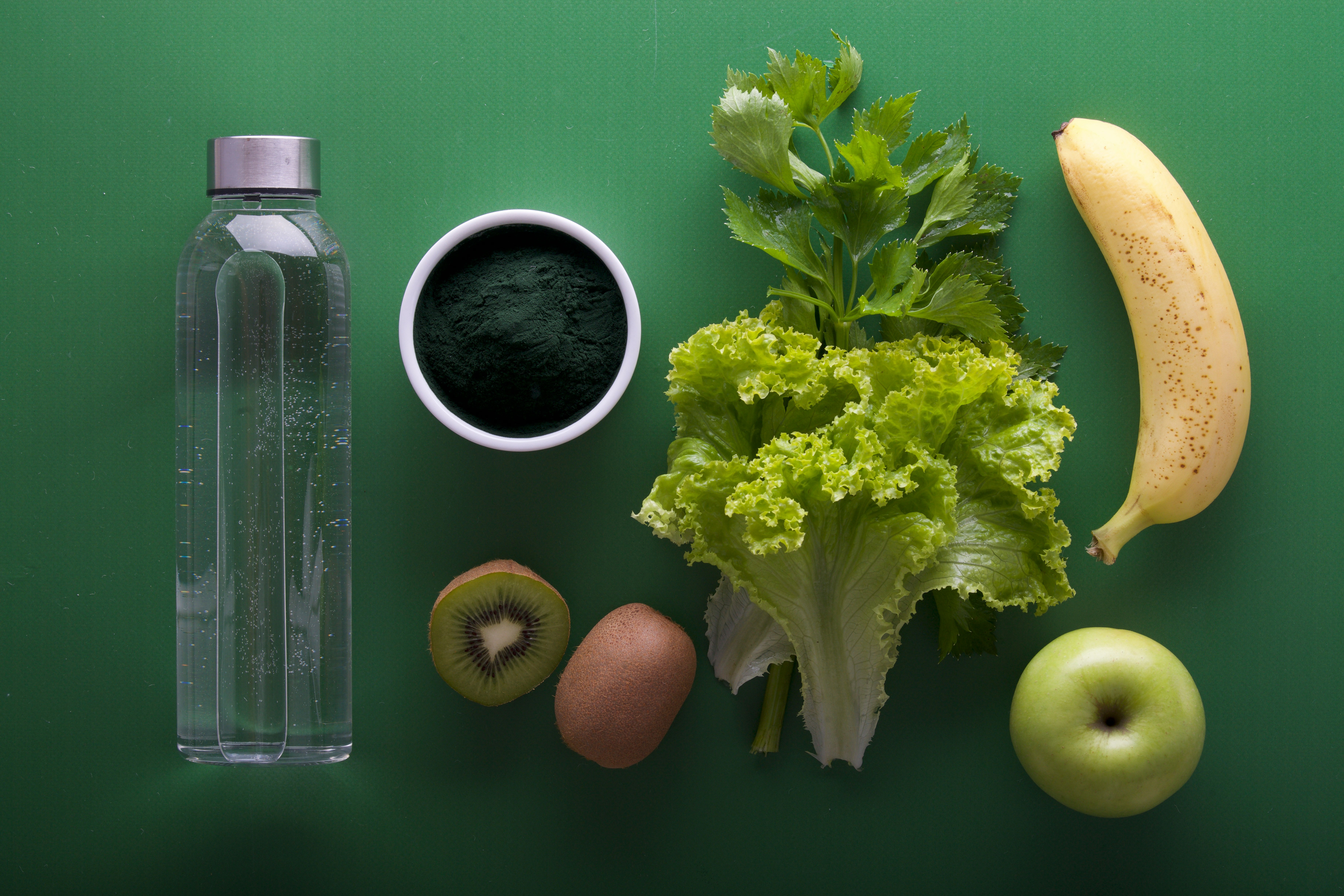 Various fruits and vegetables, including a bottle of water, arranged on a green surface.