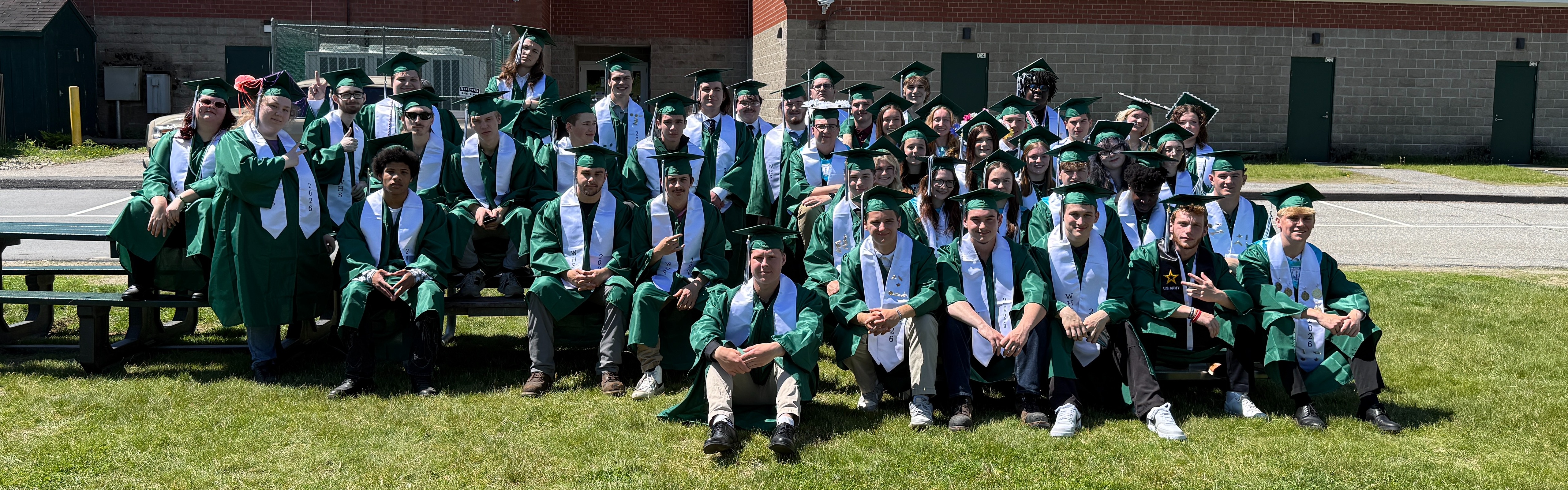 graduating class of 2026 sitting outside of school on lawn
