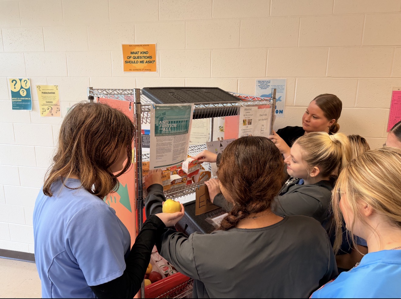 Students in blue and gray clothes looking at a project that has papers on it