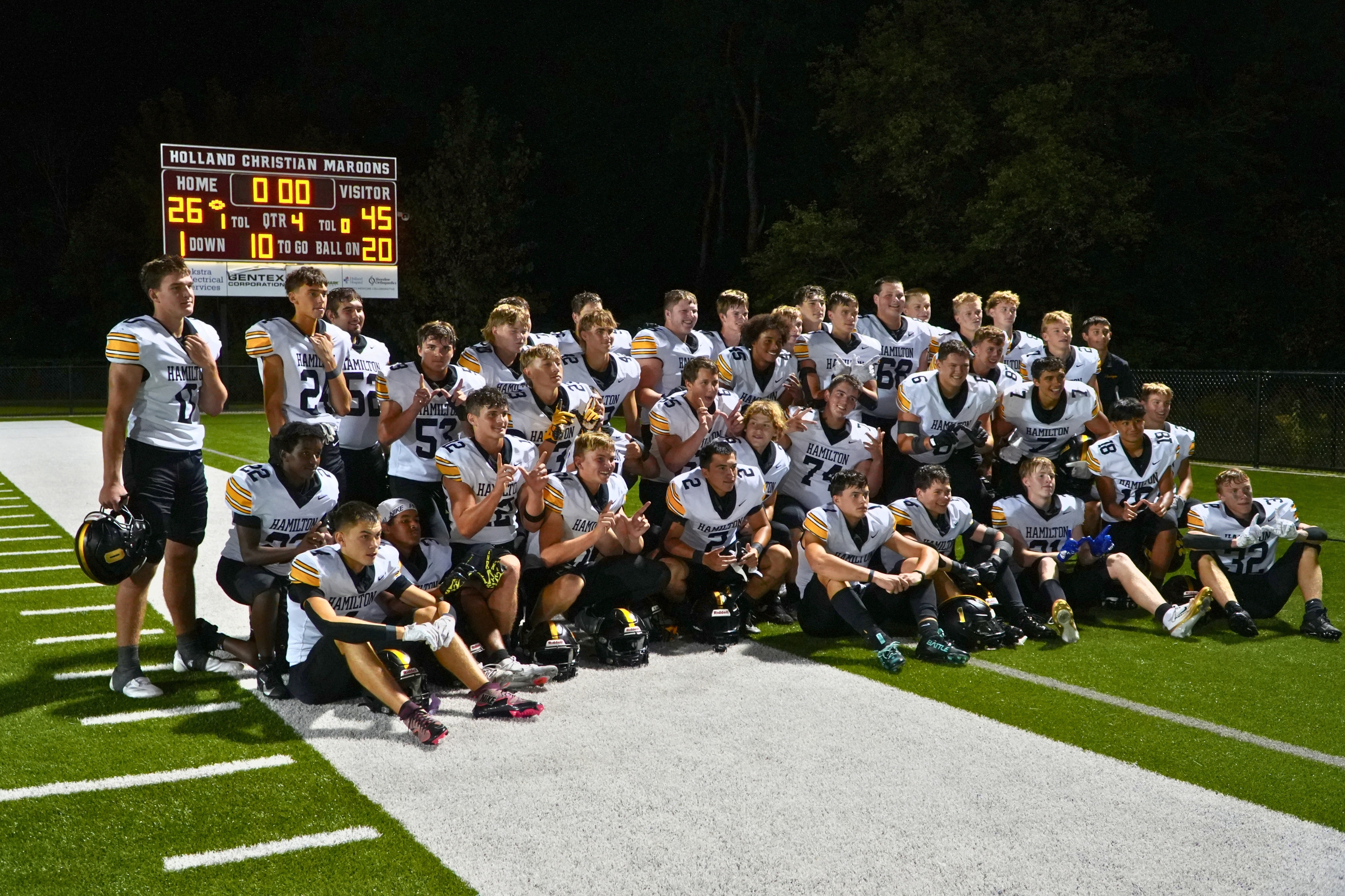 The Hamilton football team in front of a scoreboard that reads 45-26.