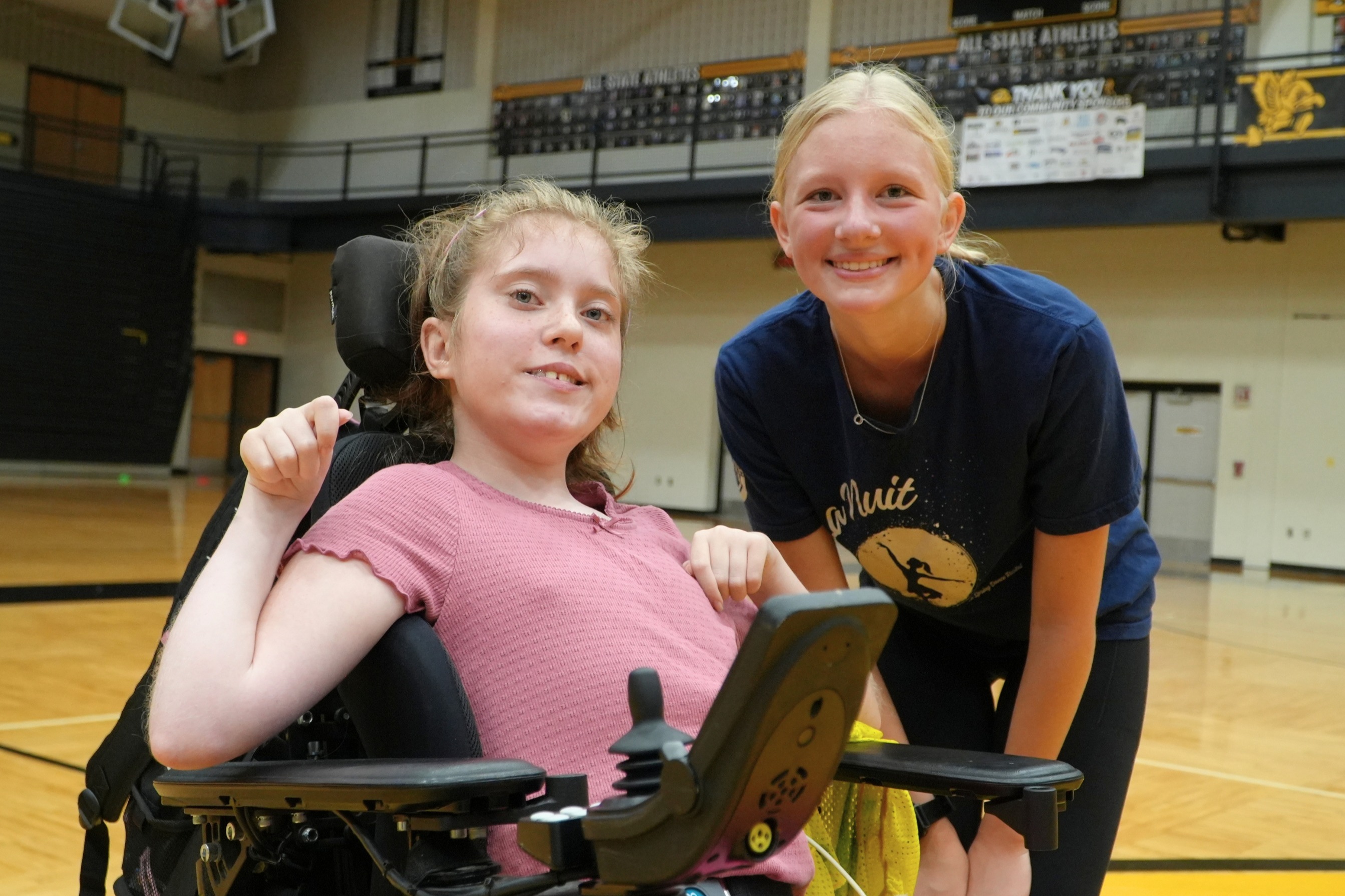 Two female students in a gymnasium smile.