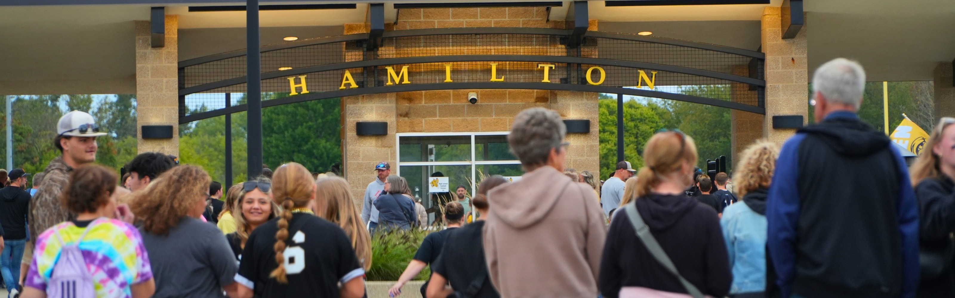 A crowd walks towards a stadium with an arch that reads 'Hamilton'.