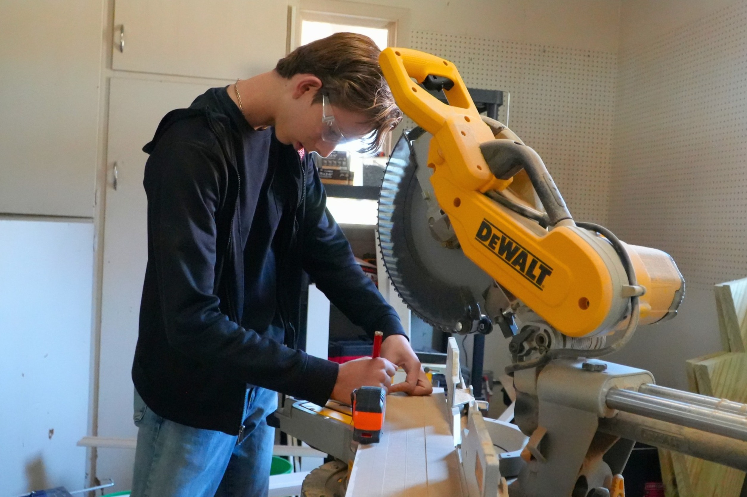 A male student uses a pencil with a yellow DeWalt saw in the photo.