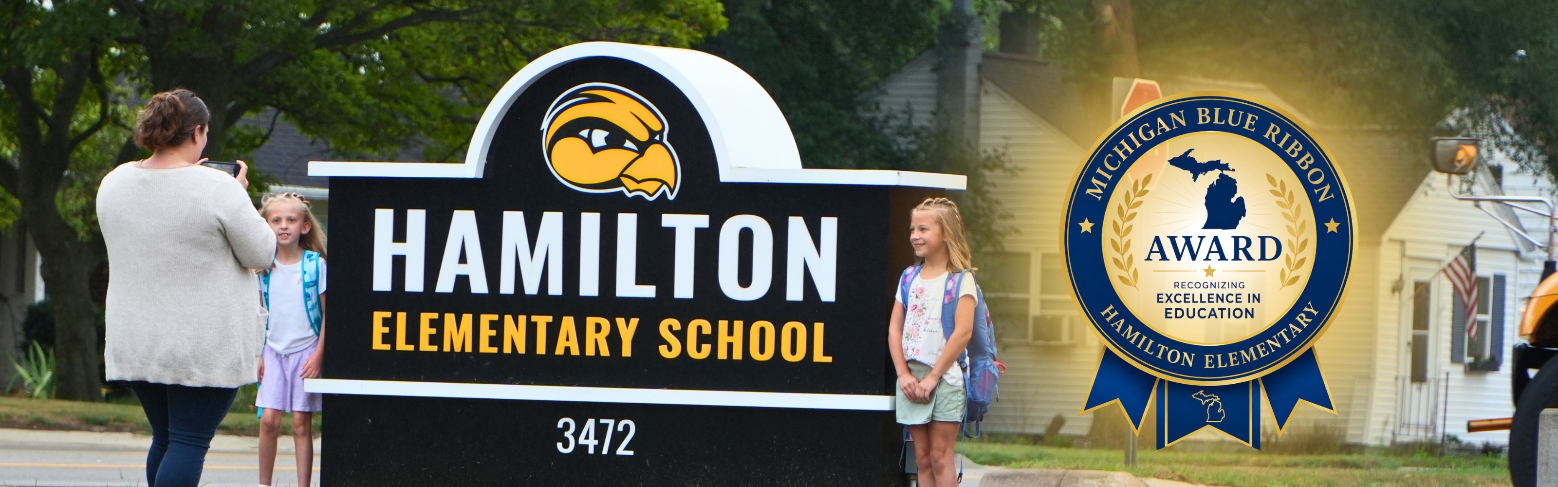 A Hamilton Elementary school sign with two female students next to it smiling.