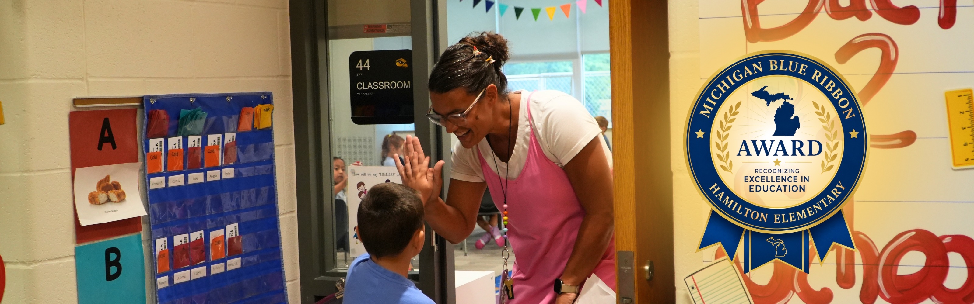 A female teacher high fives a male student entering the classroom.