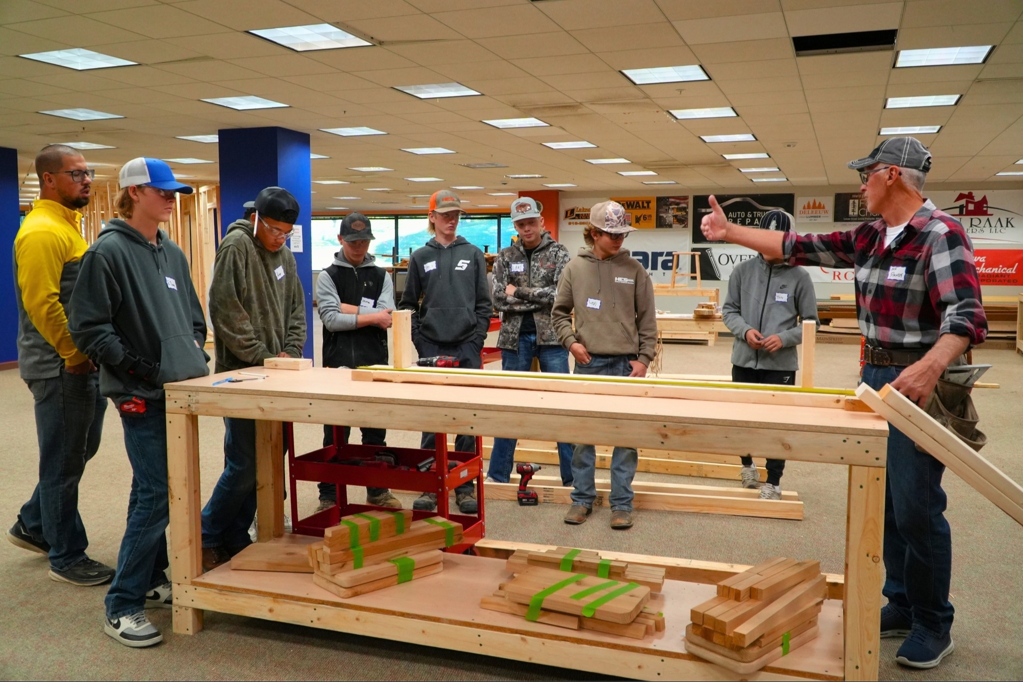 A group of male students stands around a table looking at wood and measurements.