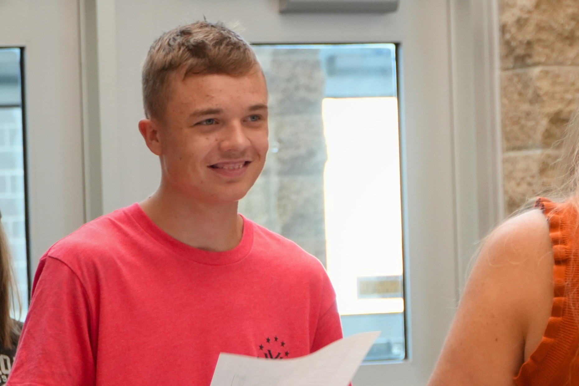 A male student smiles with a piece of paper in his hands.