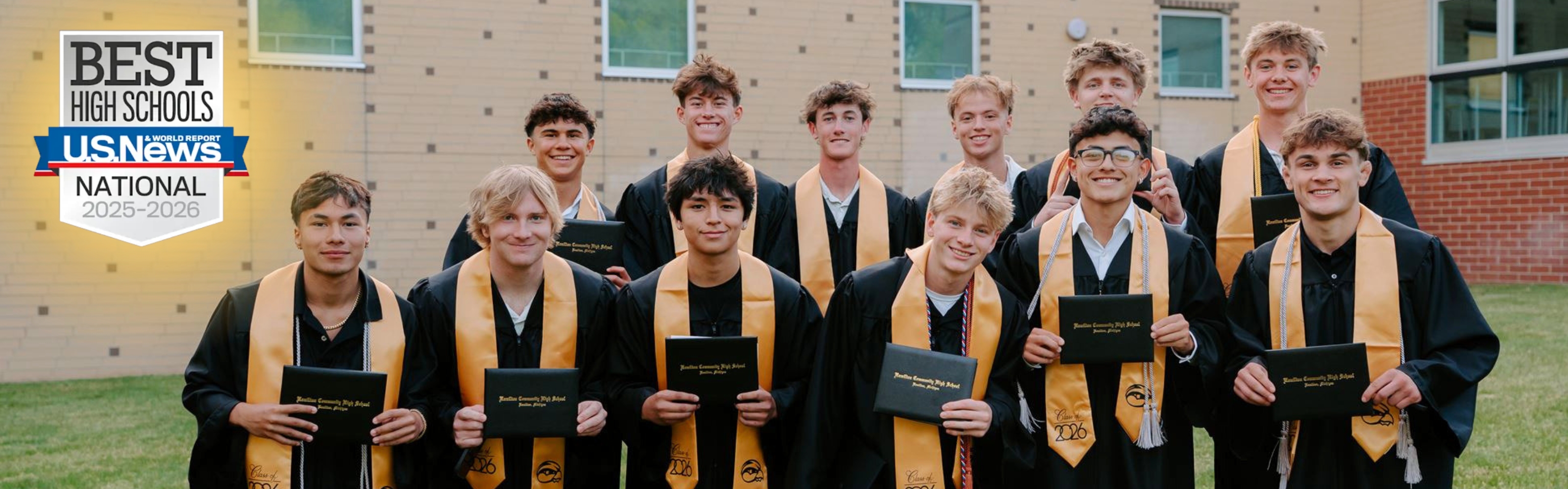 A group of male graduate students stand in front of a brick school in black and gold.
