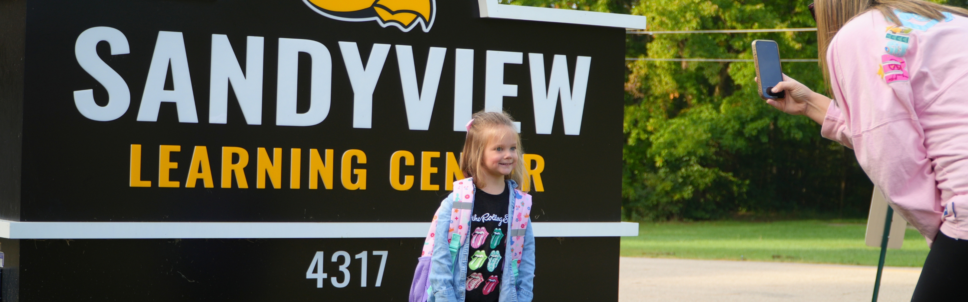 A female student smiles in front of the school sign.