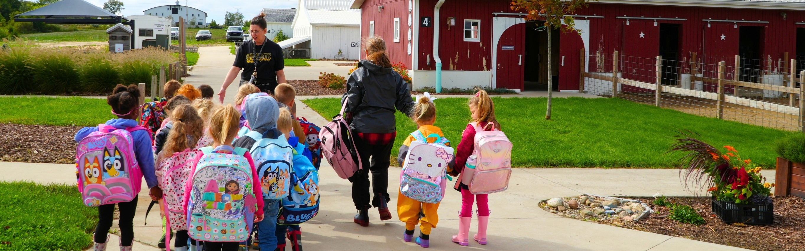 A group of female students walk with two female staff members on a farm with a big red barn.