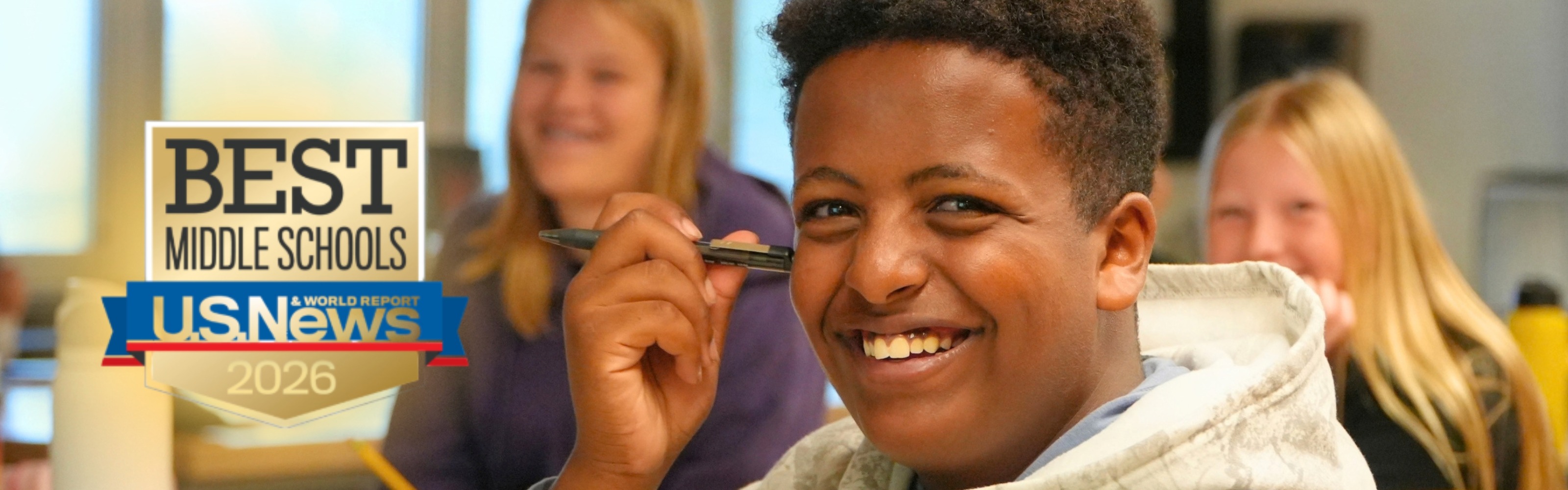 A male student smiles with a pen next to his face.