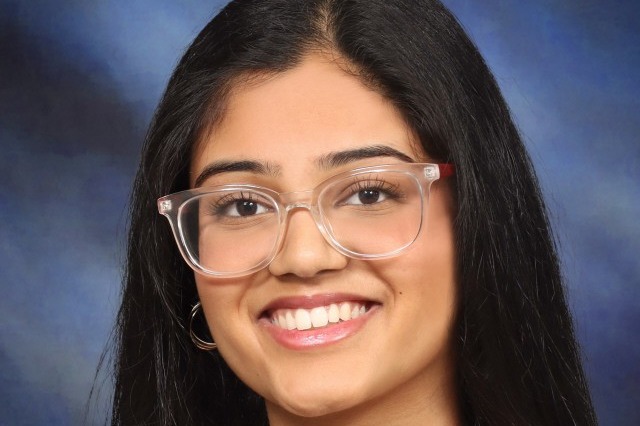 Woman with long, straight hair wearing glasses, a black top, and a necklace. She smiles.