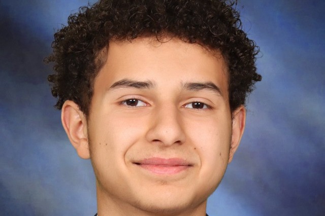 A person with curly hair smiles, wearing a black tuxedo, white shirt, and black bow tie.