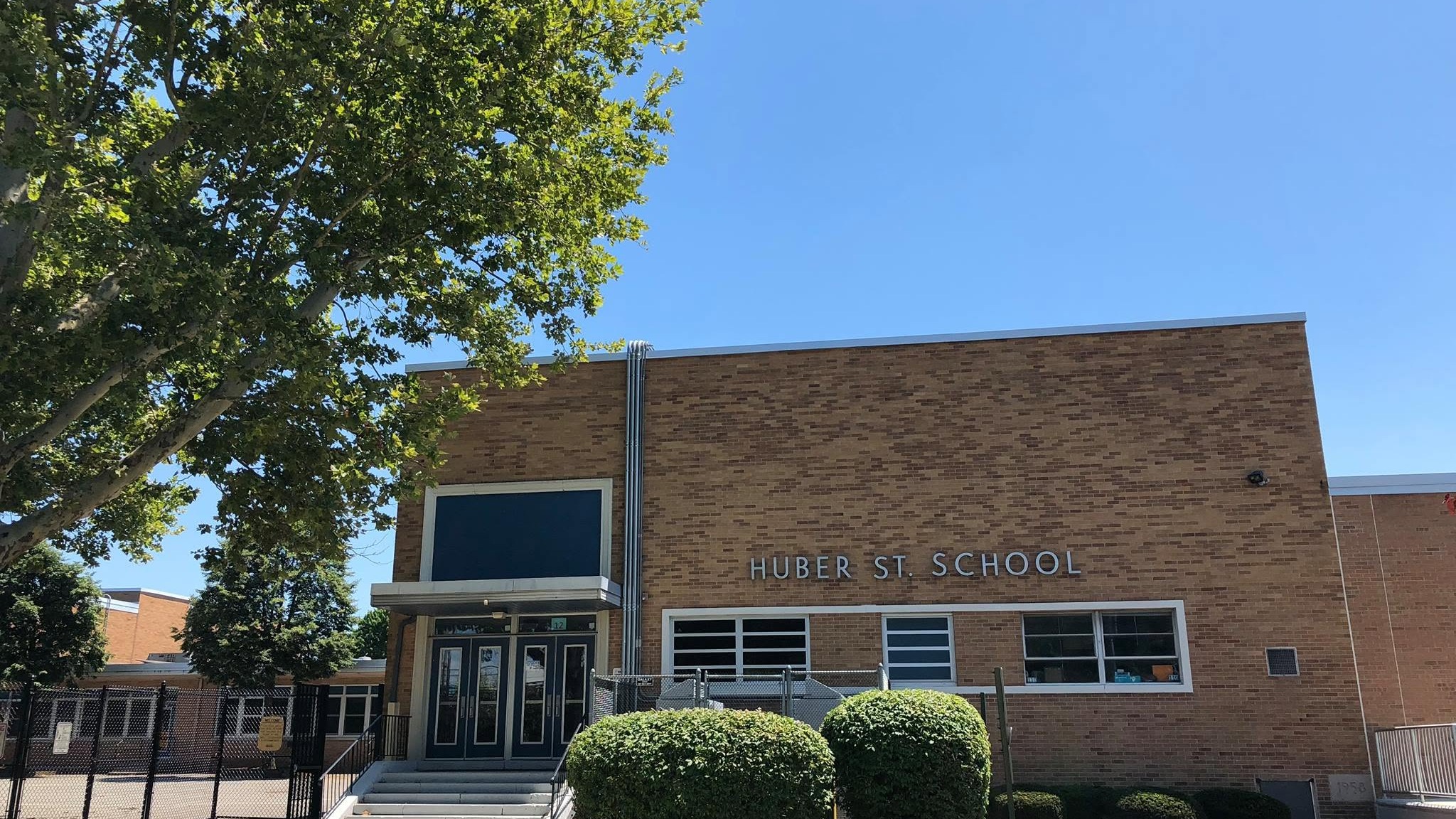 A brown brick building with a white fence and a tree in front. Text reads "Cumberland School".