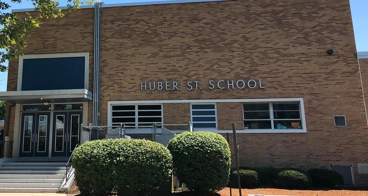 A brick building with a large entrance and steps. The sign reads "University School". Bushes are in front.
