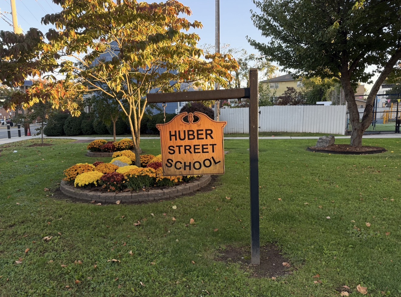 Sign for Huber Street School. Sign is wooden with a small oval bed of flowers in front.