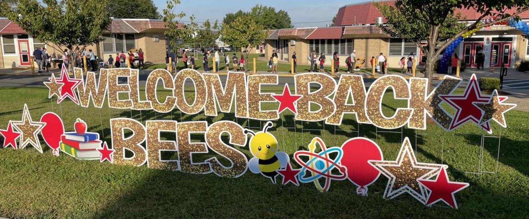 A grassy area with a sign that reads "Welcome Back Bees" decorated with stars, balloons, and other items.