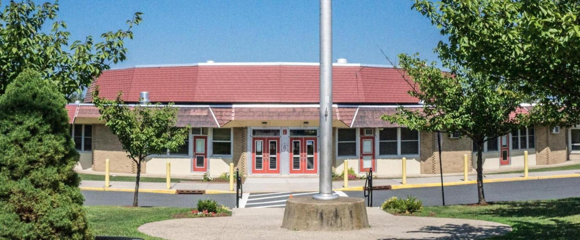A school building with a red roof and red doors. It is surrounded by trees and greenery.