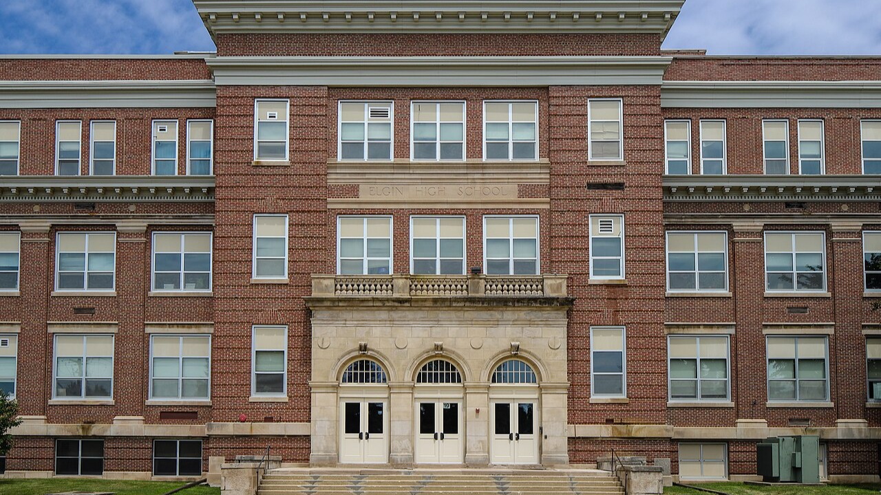 A brick building with many windows and two arched entrances. A clear blue sky with clouds in the background.