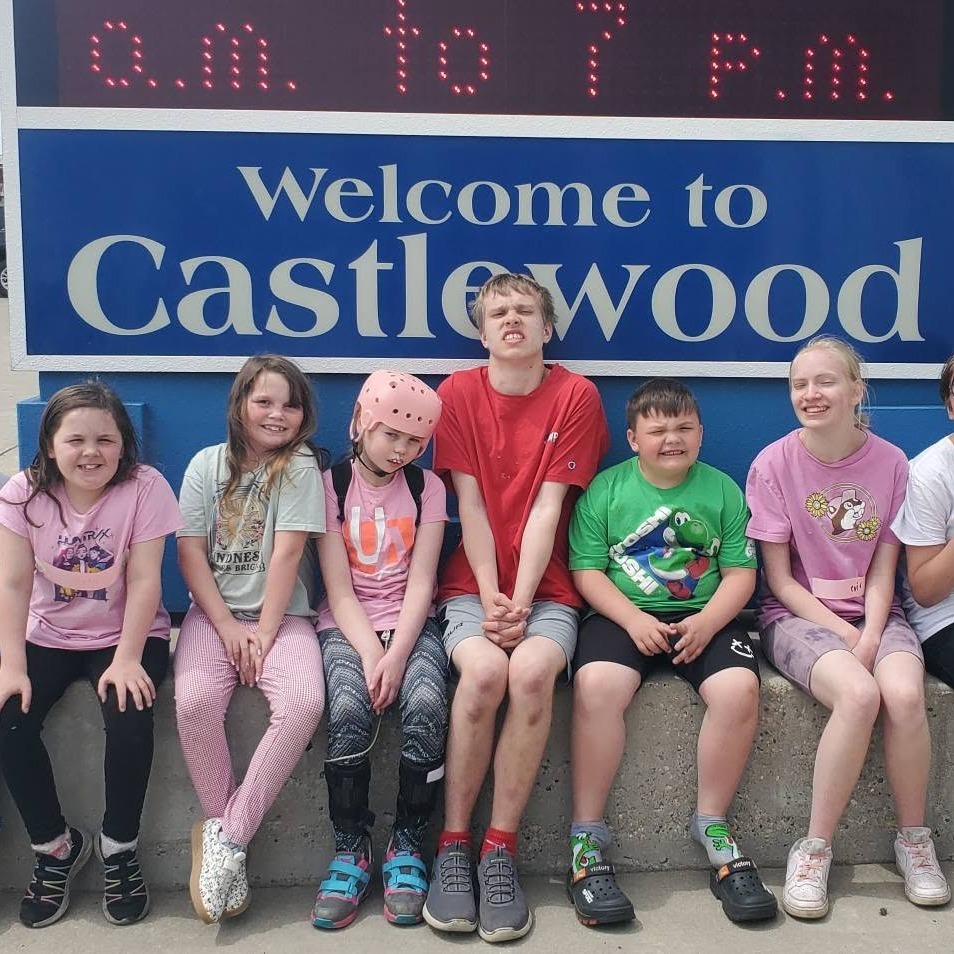 5 students of varying ages sitting in front of a school sign that says Castlewood