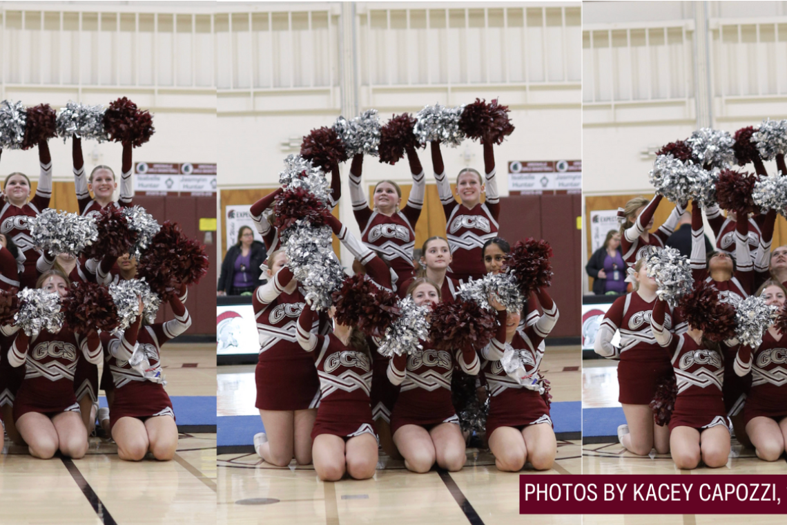A cheerleading team in maroon uniforms with silver pom-poms poses on a basketball court.