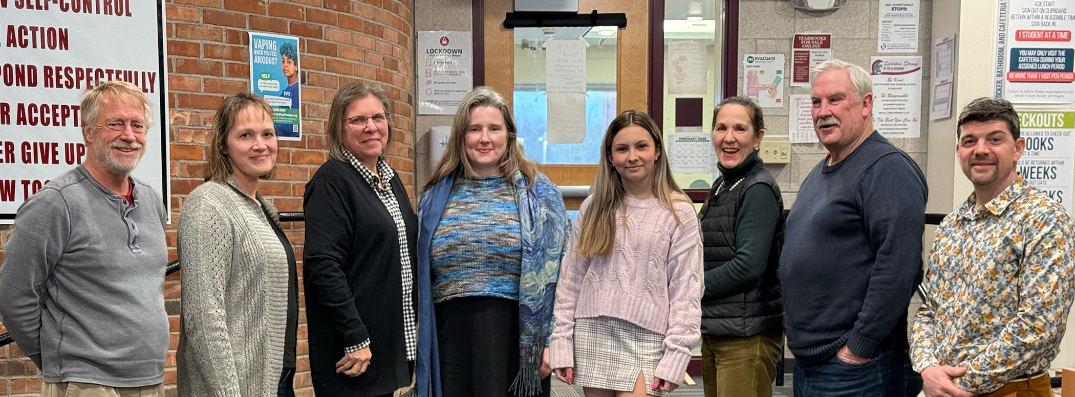 A group of seven adults and a child stand on stairs in front of a brick wall.