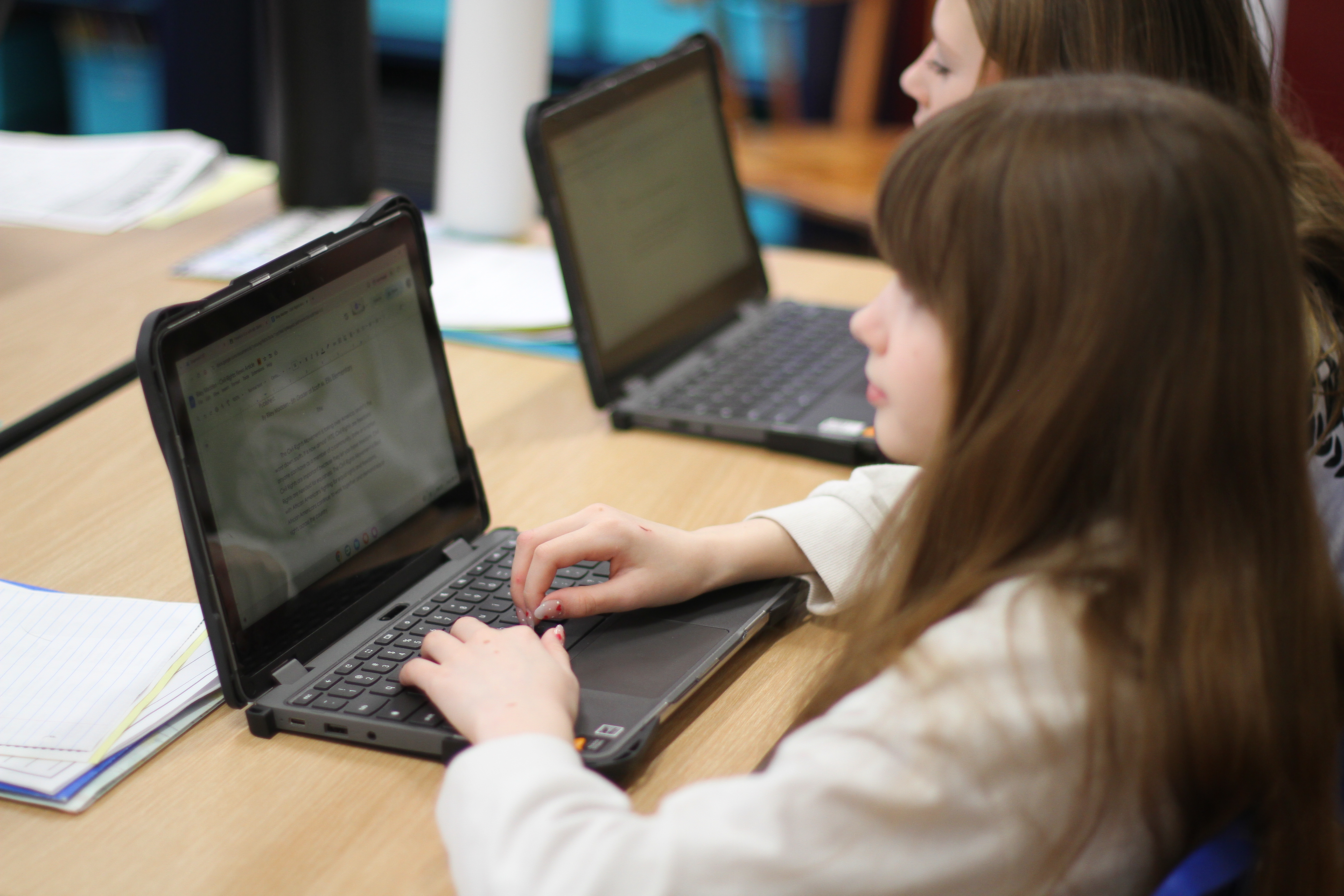 A person sitting at a desk typing on a laptop. A person with brown hair is seated at a table.
